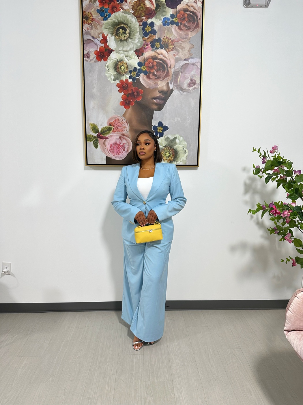 Vanessa in a light blue suit with a yellow bag in front of a floral painting