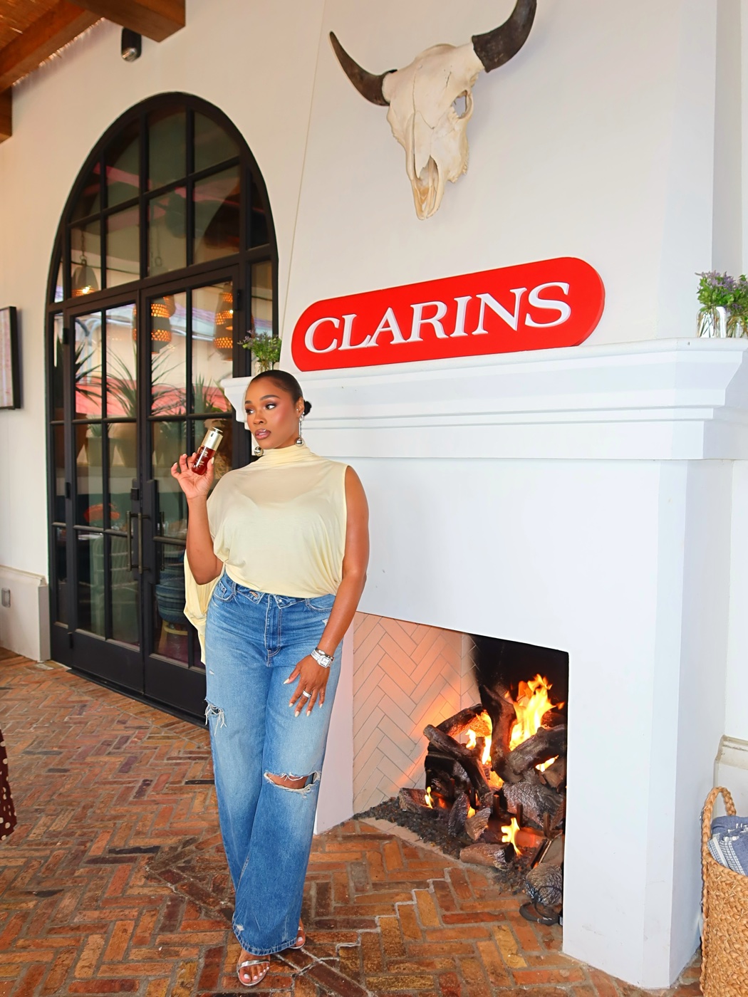 Vanessa holding a Clarins product beside a fireplace with the Clarins sign