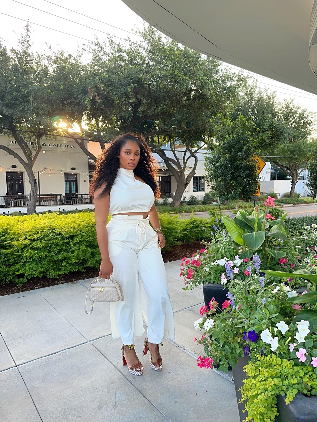 Vanessa in a white two-piece outfit with a white bag, outdoors among flowers